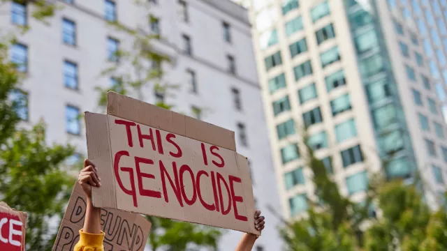 Women holding sign "this is genocide" written in red marker